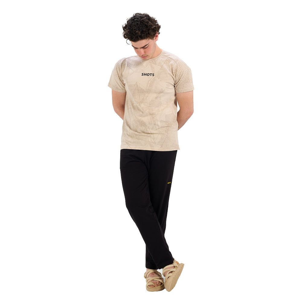 Person wearing a beige t-shirt with 'SHOTS' logo and black pants on a white background