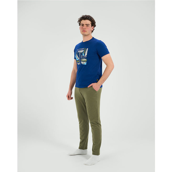 Man wearing a blue t-shirt with a graphic design and green pants on a white background